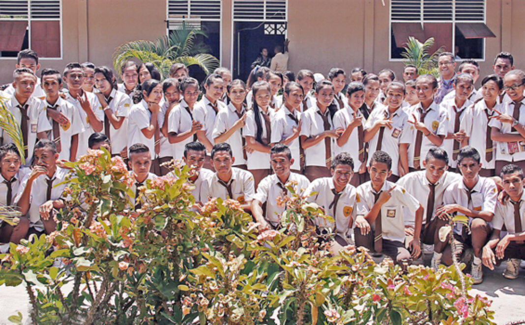 Panorama luas gedung sekolah SMP Katolik St. Maria dengan arsitektur kolonial bergaya Katolik, tamannya hijau raya, siswa-siswi berpakaian seragam putih-biru sedang belajar di luar ruangan di bawah langit cerah dengan pohon-pohon rindang dan background gunung yang indah, gaya foto realistis dengan pencahayaan alami sore hari